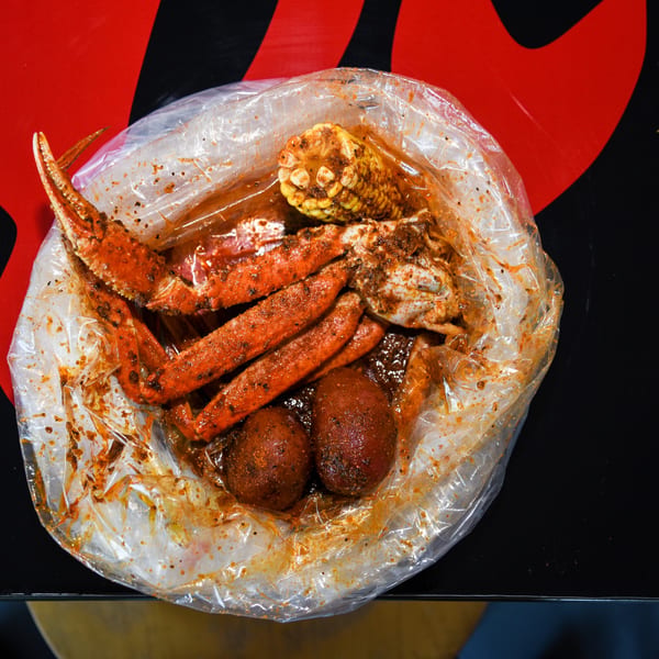 Bluff City Crab's seafood boil with crab legs, corn, and potatoes in a clear plastic bag.