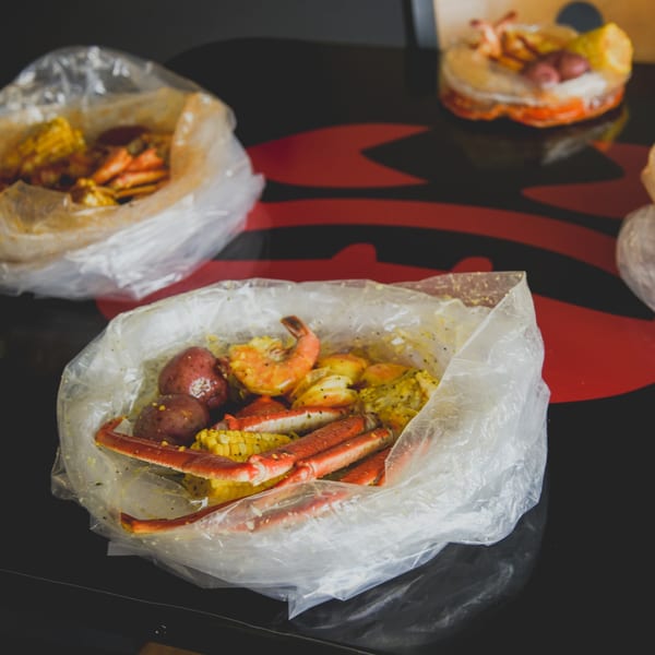 Bluff City Crab seafood boil bags with crab legs, shrimp, corn, and potatoes on a black table.