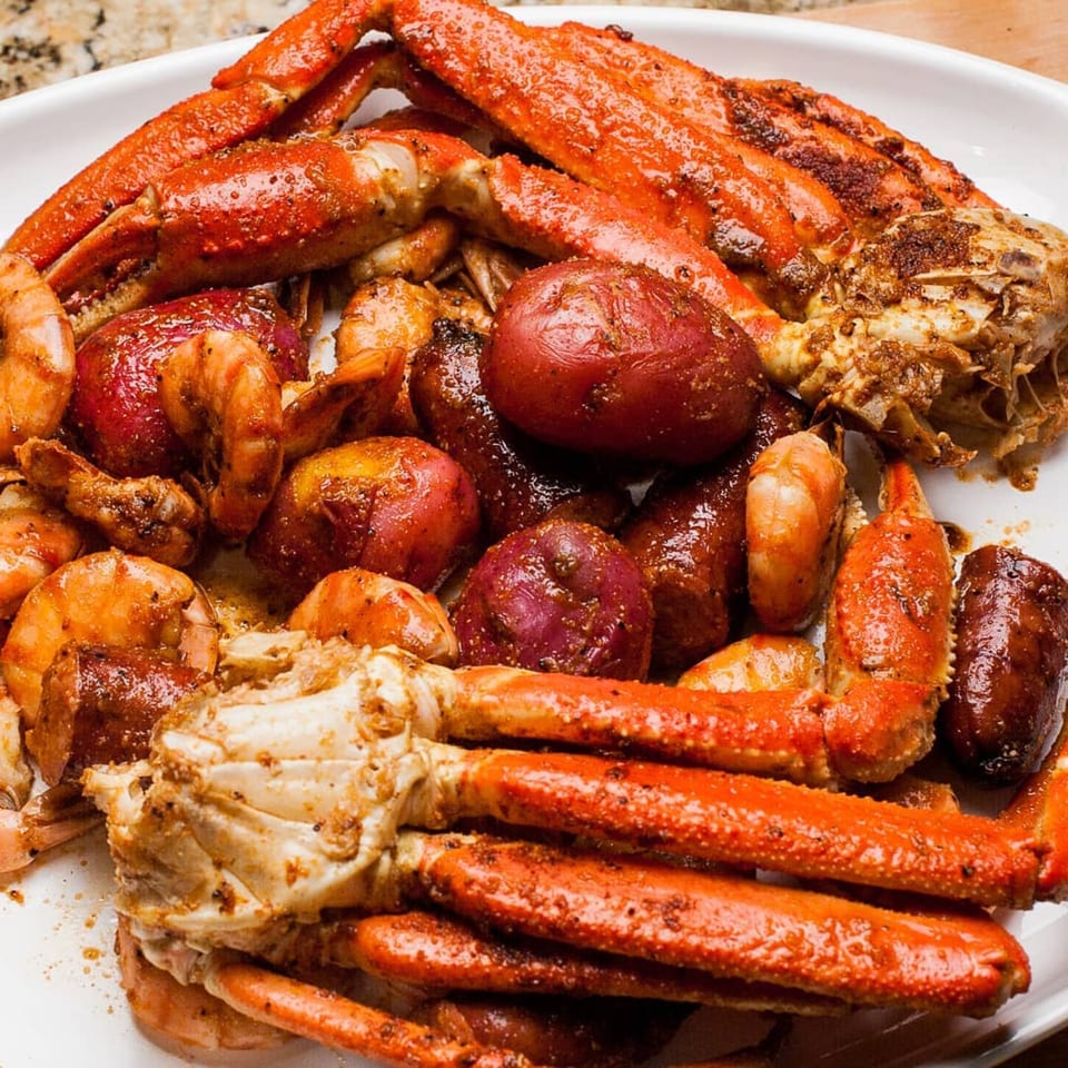 A white platter piled high with seasoned crab legs, shrimp, red potatoes, and sausage.